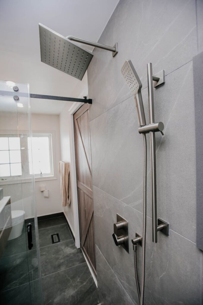 Brushed nickel square rain head and handheld shower on a slide bar with a wood look barn door behind