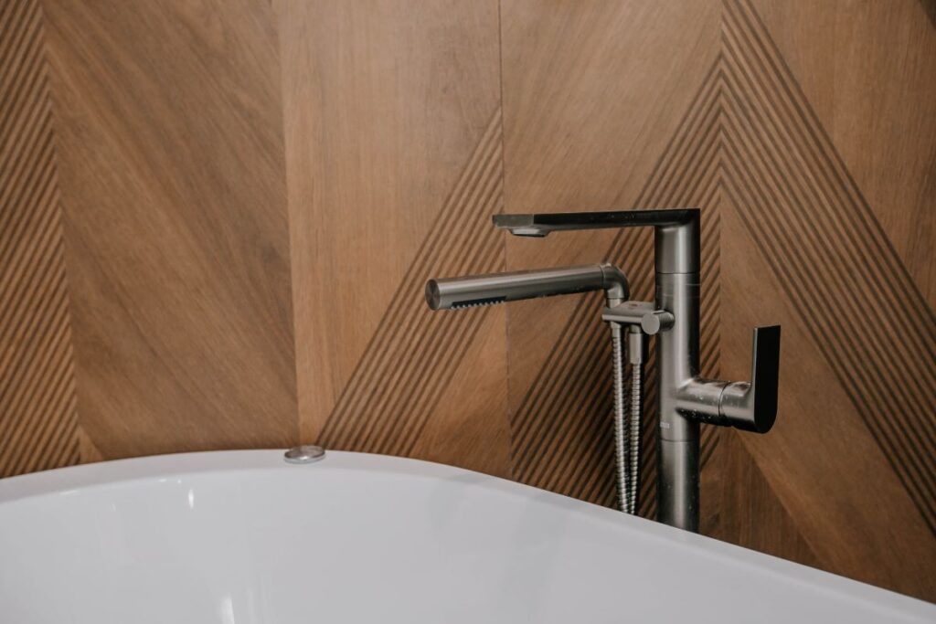 Floor mounted brushed nickel tub filler with handheld sprayer in front of a walnut chevron wood look porcelain wall