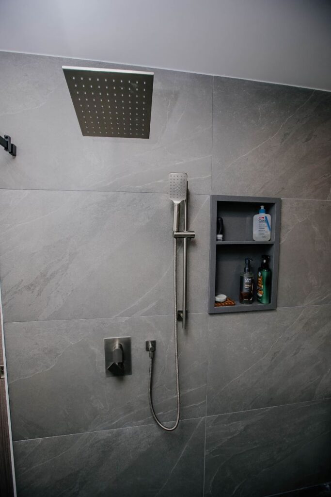 Grey stone look porcelain shower wall with a recessed double niche, square rain head and brushed nickel handheld