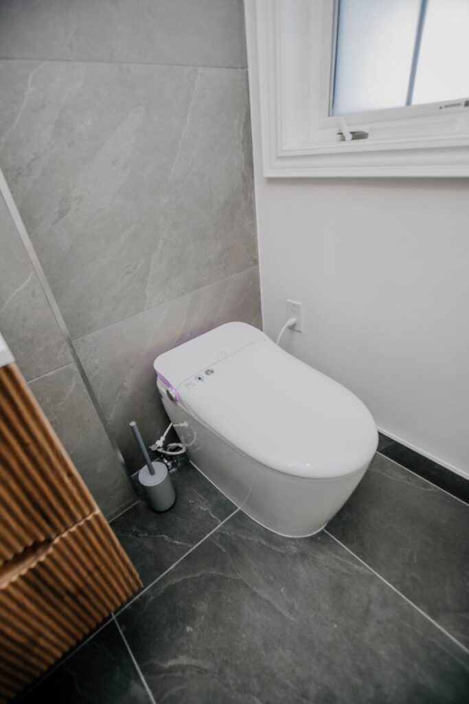 Modern smart toilet with night light on charcoal slate look porcelain floor next to a frosted window