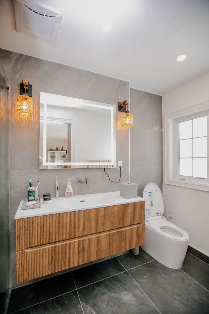 Renovated master bathroom vanity wall with fluted oak floating cabinet, LED mirror, amber rattan sconces and a smart toilet