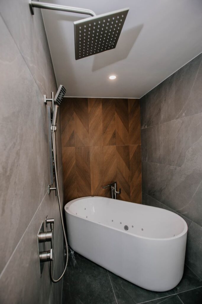 Markham Bathroom Renovation - Square brushed nickel rain shower and handheld over a freestanding soaking tub against a walnut chevron feature wall