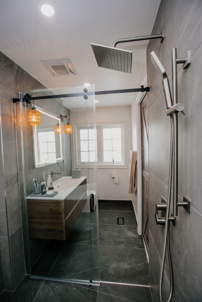 Wide view of a Markham master bathroom combined tub and shower wet area with sliding glass door, fluted oak vanity and dual rain showers