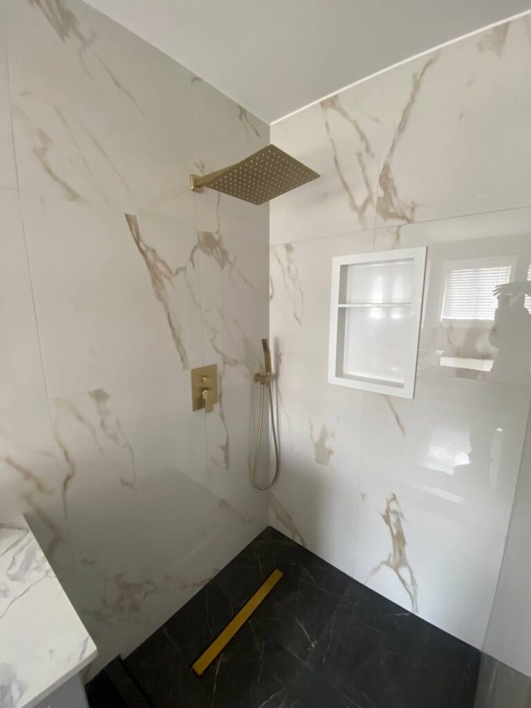 Close up view of walk in shower with large marble effect tiles gold rain showerhead and handheld shower fixture Recessed shelf built into the shower wall photo 2024 05 25 19 29 00
