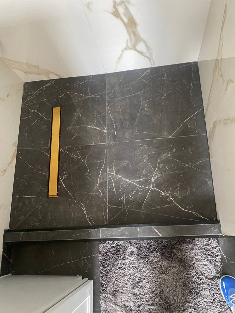 modern shower stall with dar grey marble tile floor gold linear drain and small step up to the bathroom floor photo 2024 05 25 19 30 35