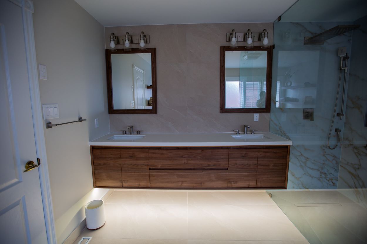 A floating custom vanity unit with natural wood fronts with LED lighting, a minimalist design, and a white countertop. Two floating dark wood shelves matching the vanity are located above the bathtub