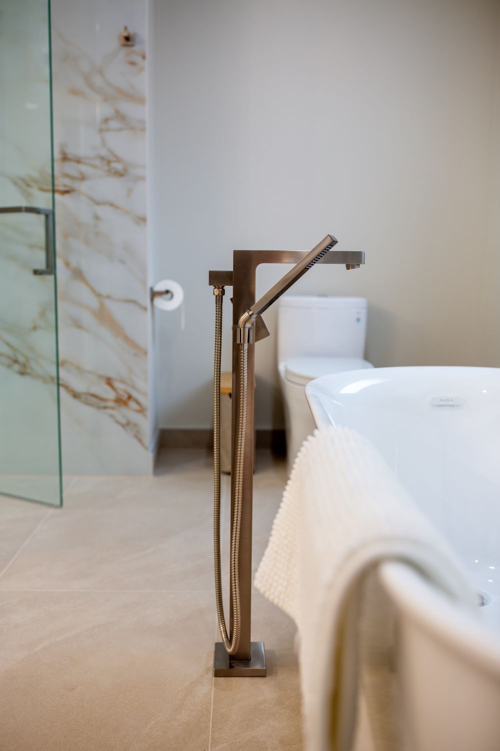 A freestanding oval bathtub of modern design, complemented by an elegant floor mounted mixer with a hand shower, all in a matching brass finish general Barrie