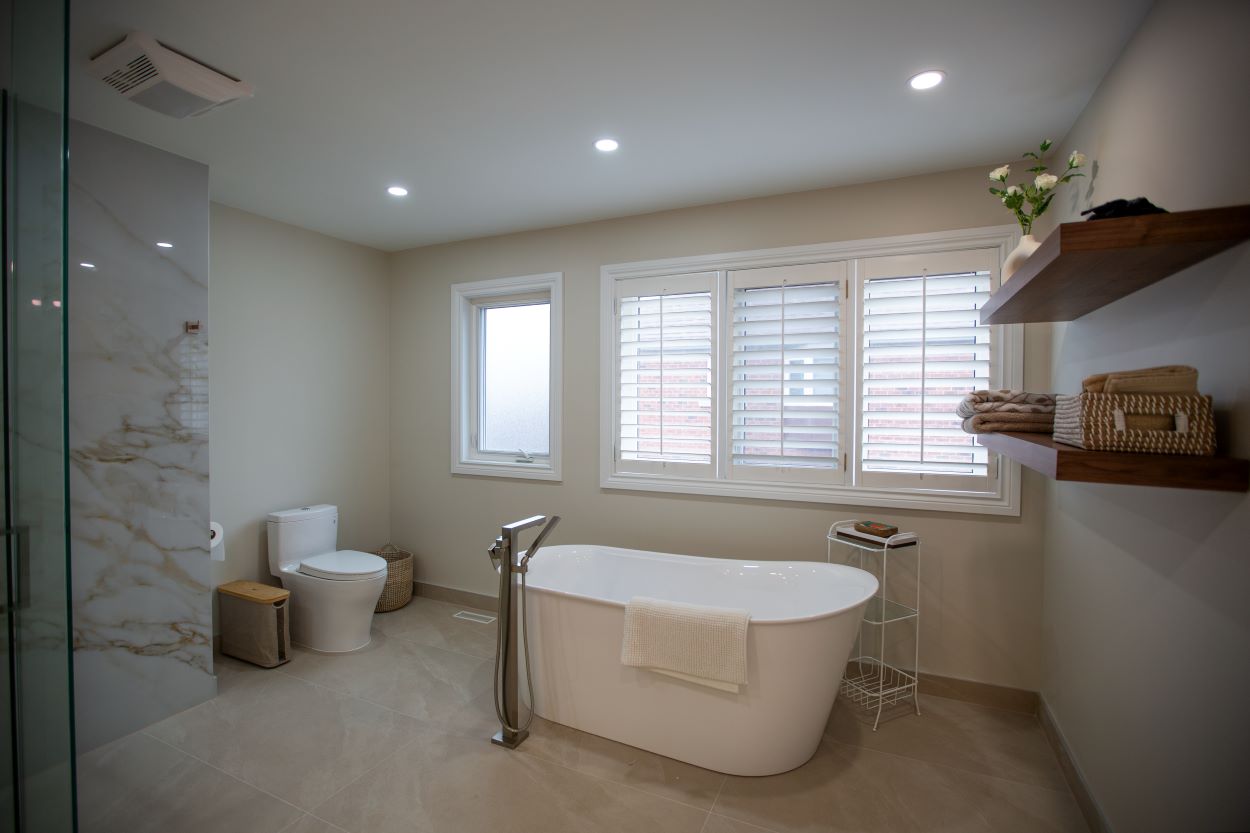 A freestanding oval bathtub of modern design, complemented by an elegant floor mounted mixer with a hand shower, all in a matching brass finish Barrie