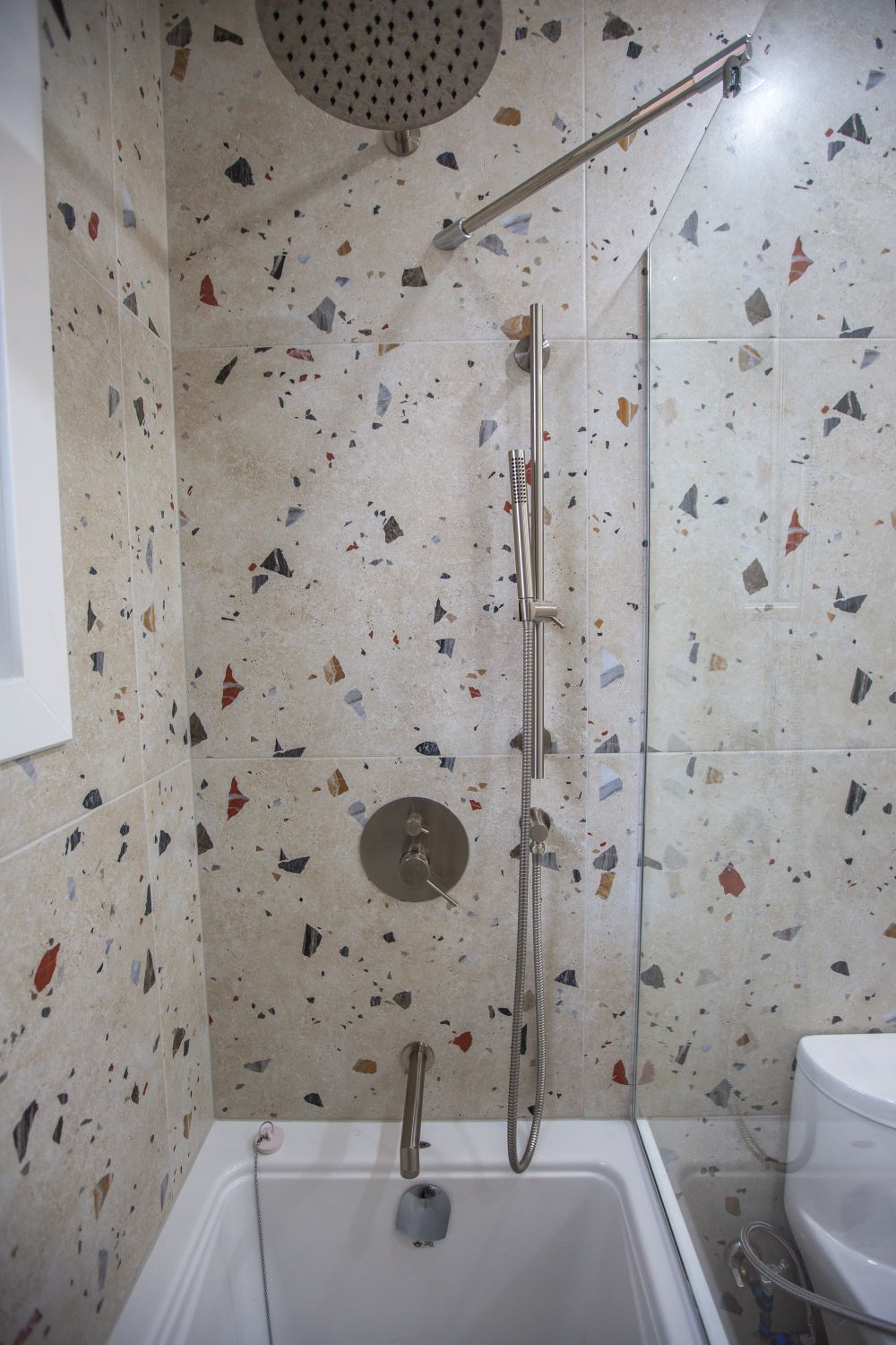 All plumbing fixtures – the modern faucet for the sink, the complete shower system (including an overhead shower, a hand shower on a bar, and a tub spout) – feature a consistent chrome finish Barrie