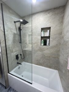 Elegant bathroom remodel with tub, beige stone look tiles, and matte black shower system
