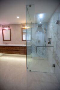 Glass Enclosure A spacious custom shower enclosure made of thick tempered glass (frameless) with a hinged door and hardware in a matching brass finish