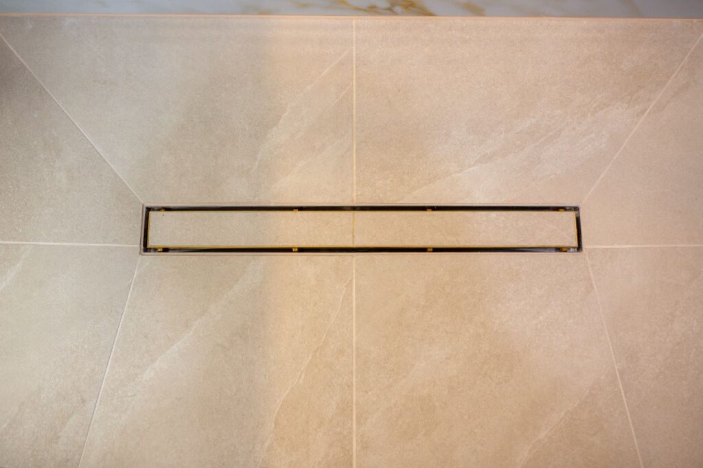 The floor throughout the bathroom is laid with large format tiles in a neutral shade. The shower area features a modern linear drain with high precision tile fitting