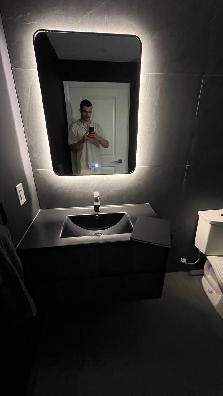 Modern dark bathroom vanity area with a floating reeded cabinet, integrated matte black sink, and an LED backlit mirror with touch controls