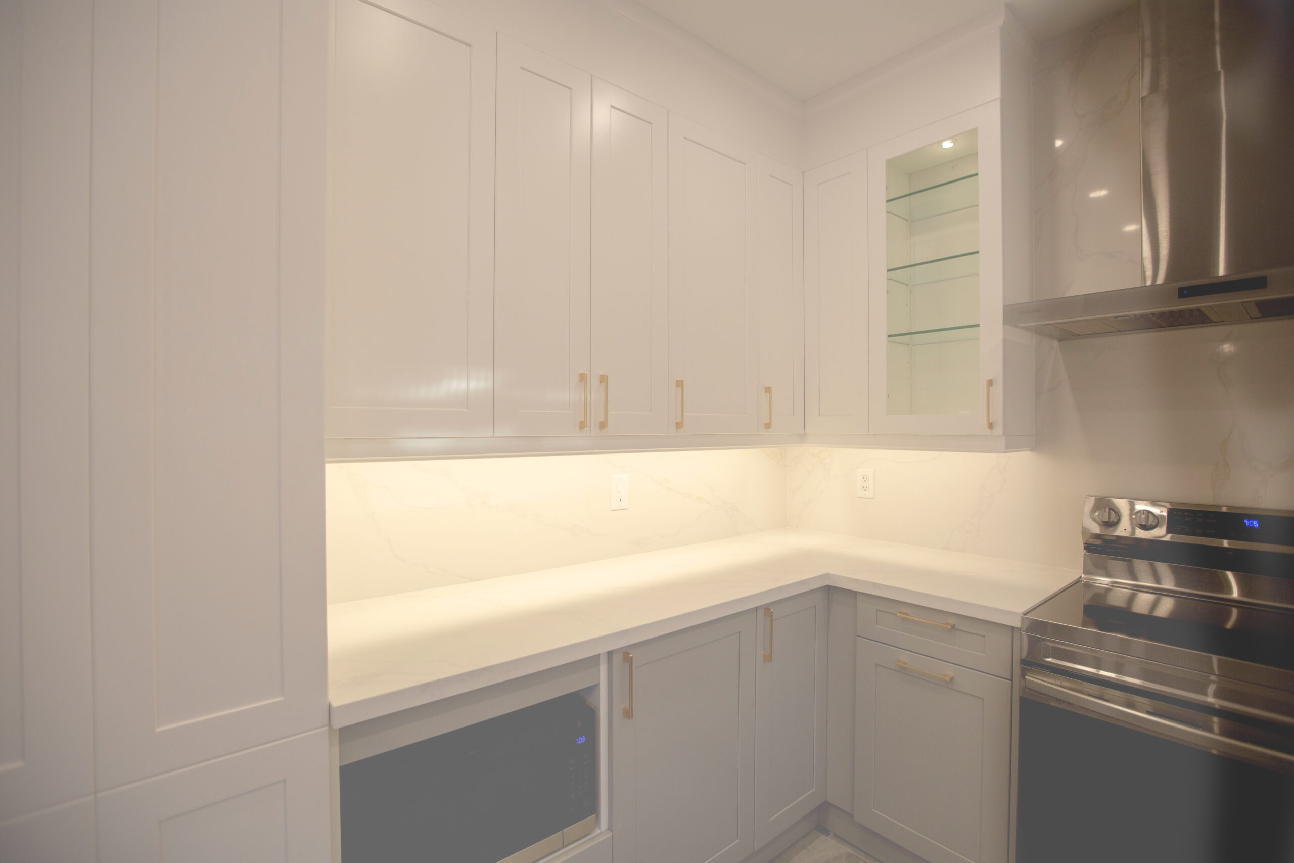 Bright modern kitchen renovation in Pickering featuring white matte cabinetry, quartz countertops, clean tile backsplash, and stainless steel hood