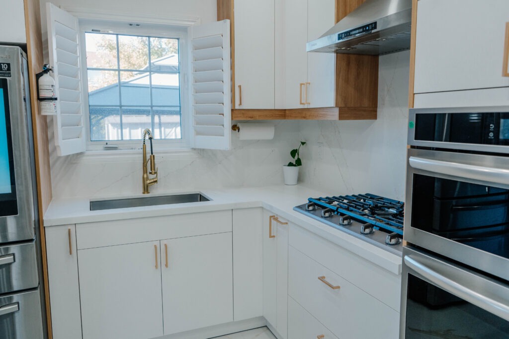 Bright sink and cooktop area in the Deluxe Style kitchen, featuring a gold faucet, undermount sink, and white flat panel cabinetry