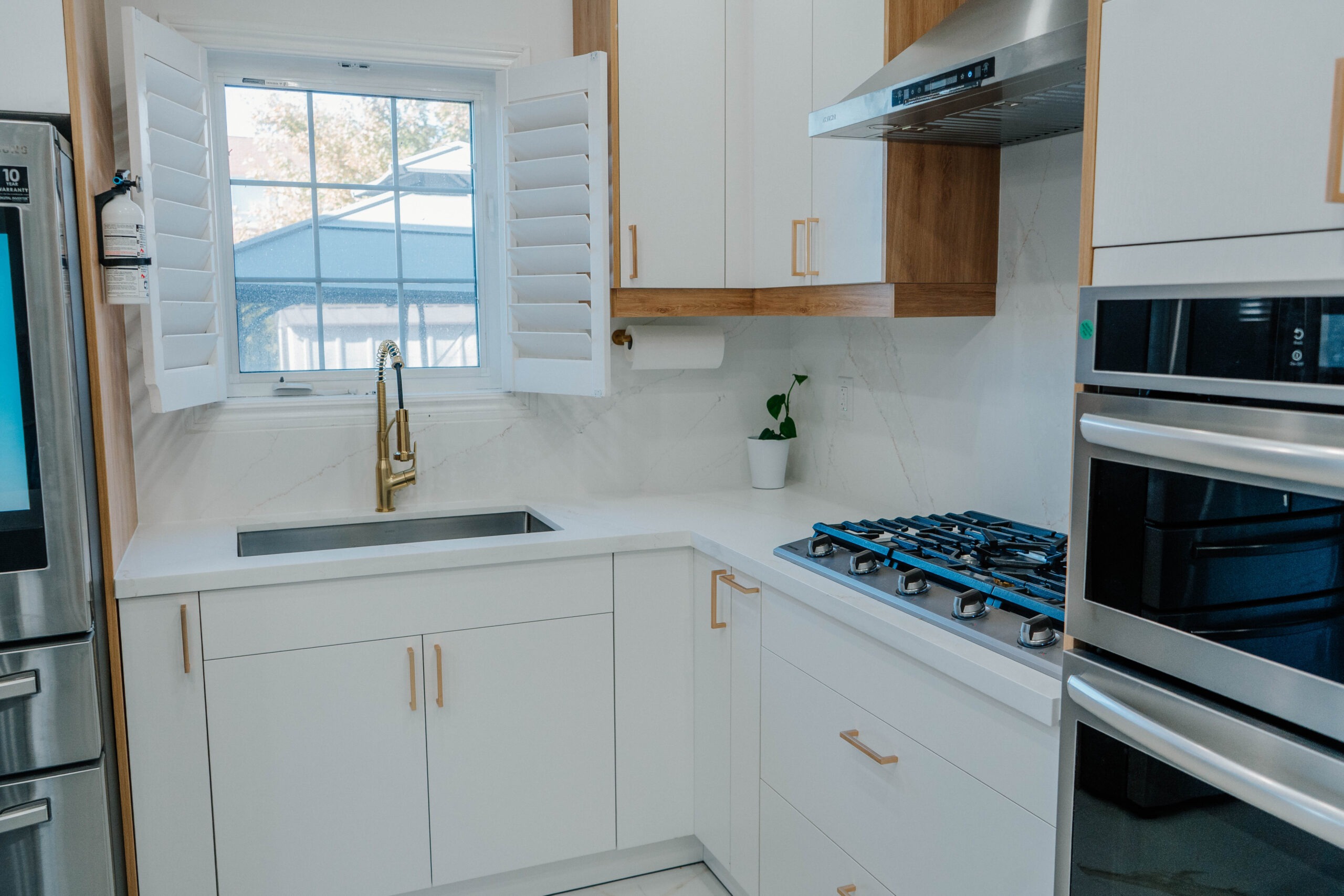 Bright sink and cooktop area in the Deluxe Style kitchen, featuring a gold faucet, undermount sink, and white flat panel cabinetry