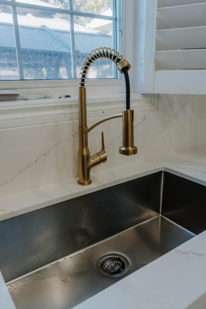 Close up of the modern gold kitchen faucet and deep undermount sink, set against the elegant quartz countertop and backsplash