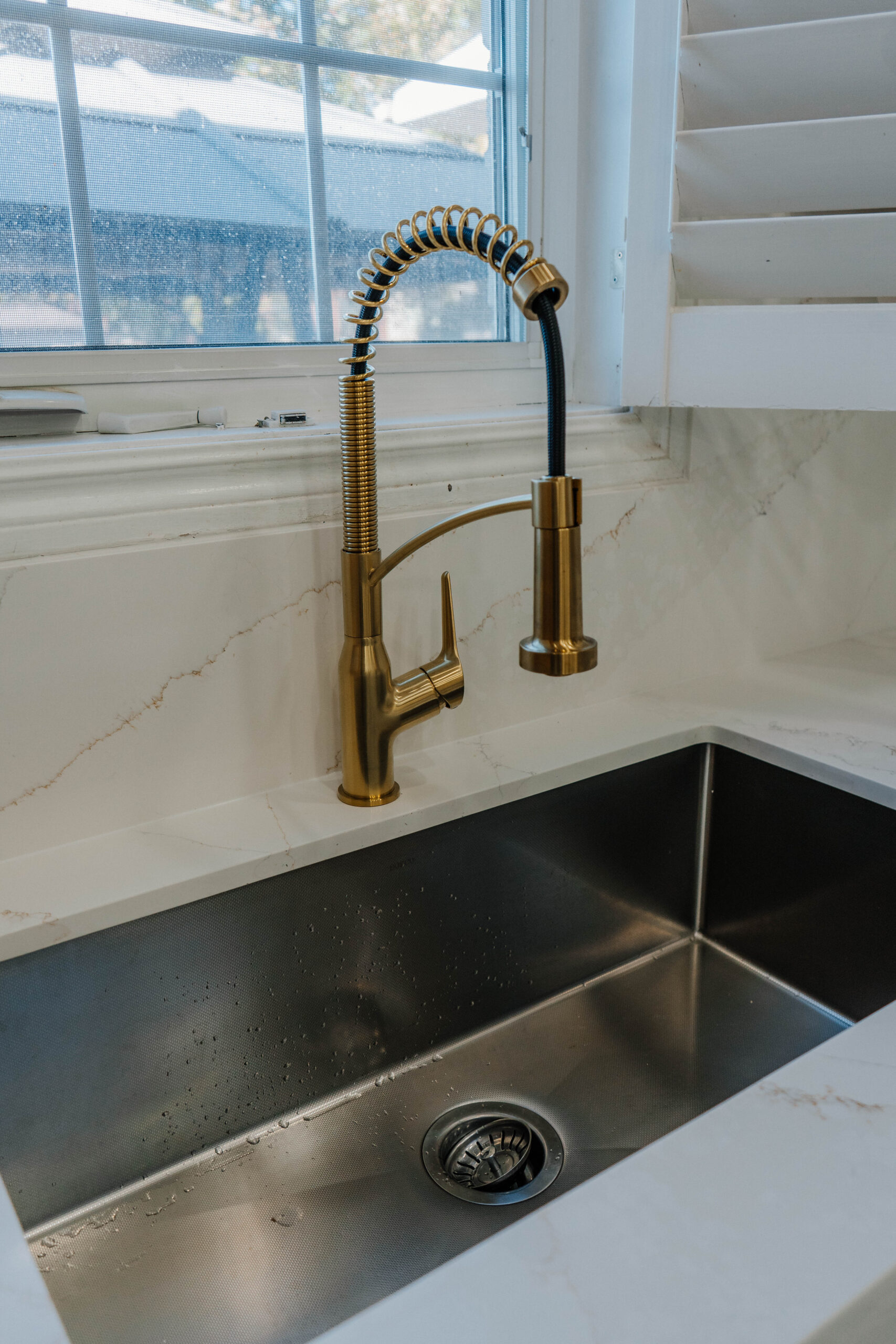 Close up of the modern gold kitchen faucet and deep undermount sink, set against the elegant quartz countertop and backsplash