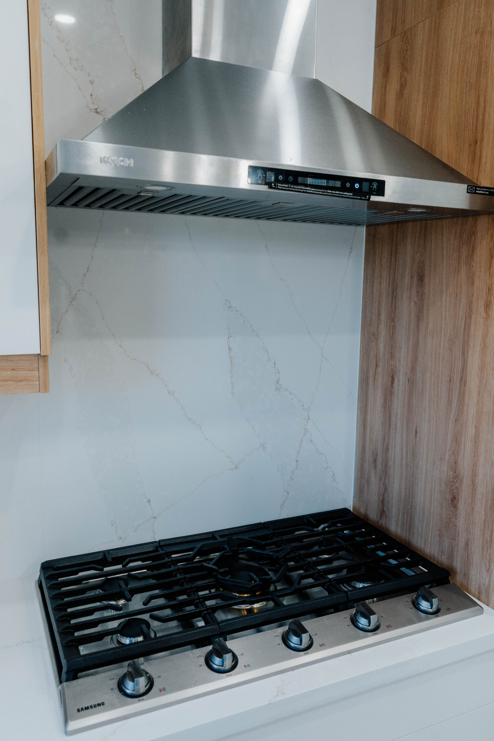 Close up of the stainless steel gas cooktop and modern range hood, with the seamless Calacatta style quartz backsplash in the background Pickering