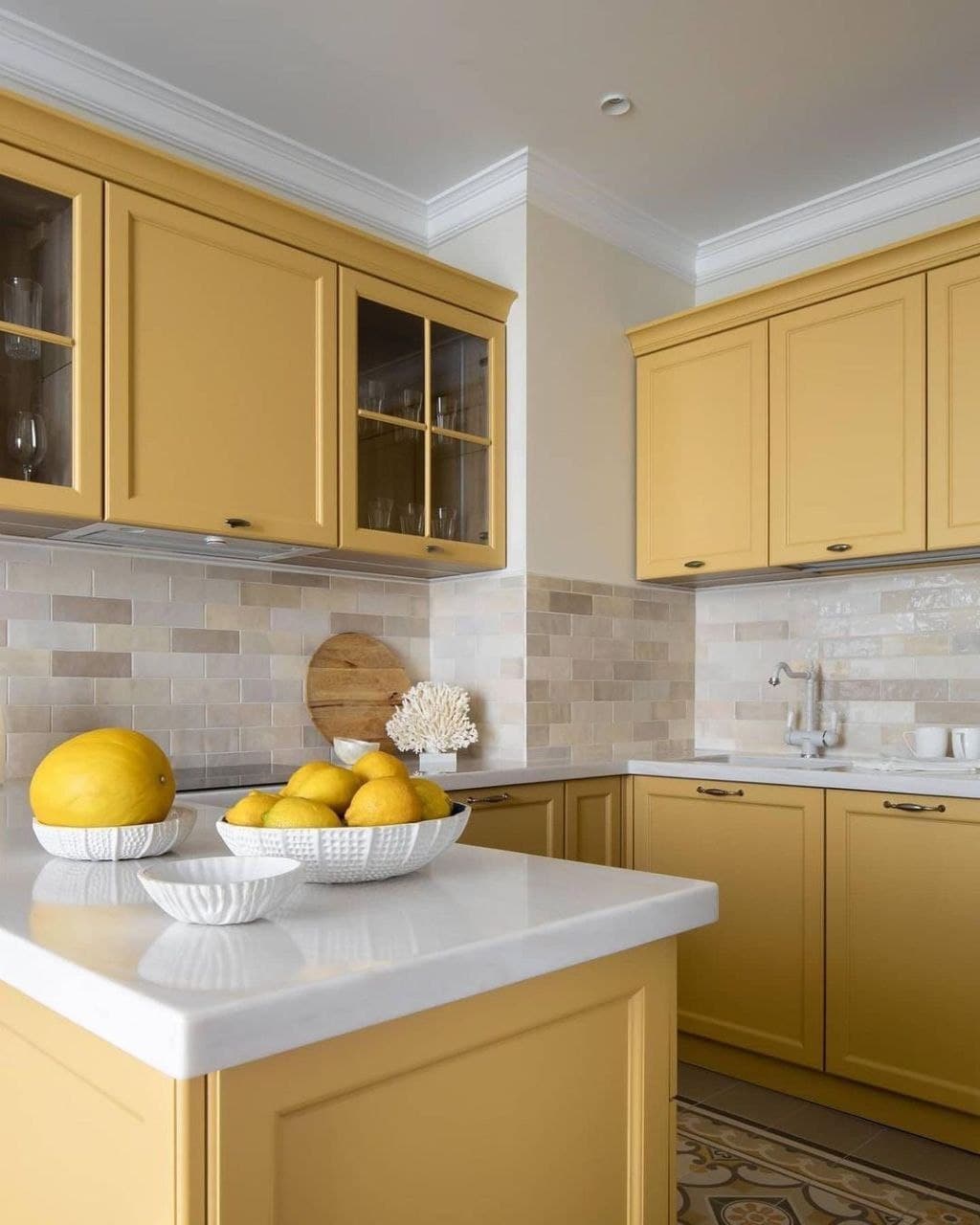 Close up of yellow kitchen cabinets featuring glass front uppers, white countertop, and beige brick backsplash tiling Pickering
