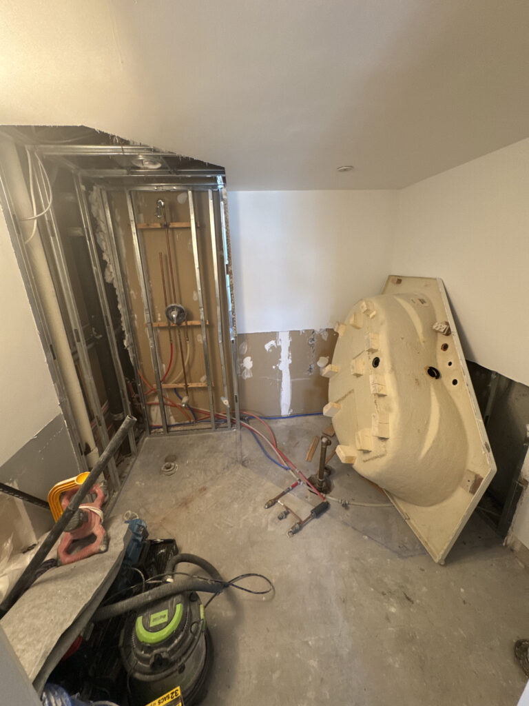 Demolition phase of a bathroom renovation. Photo shows the room stripped down to the studs, with exposed plumbing and an old, removed bathtub leaning against the wall. Construction phase in the GTA