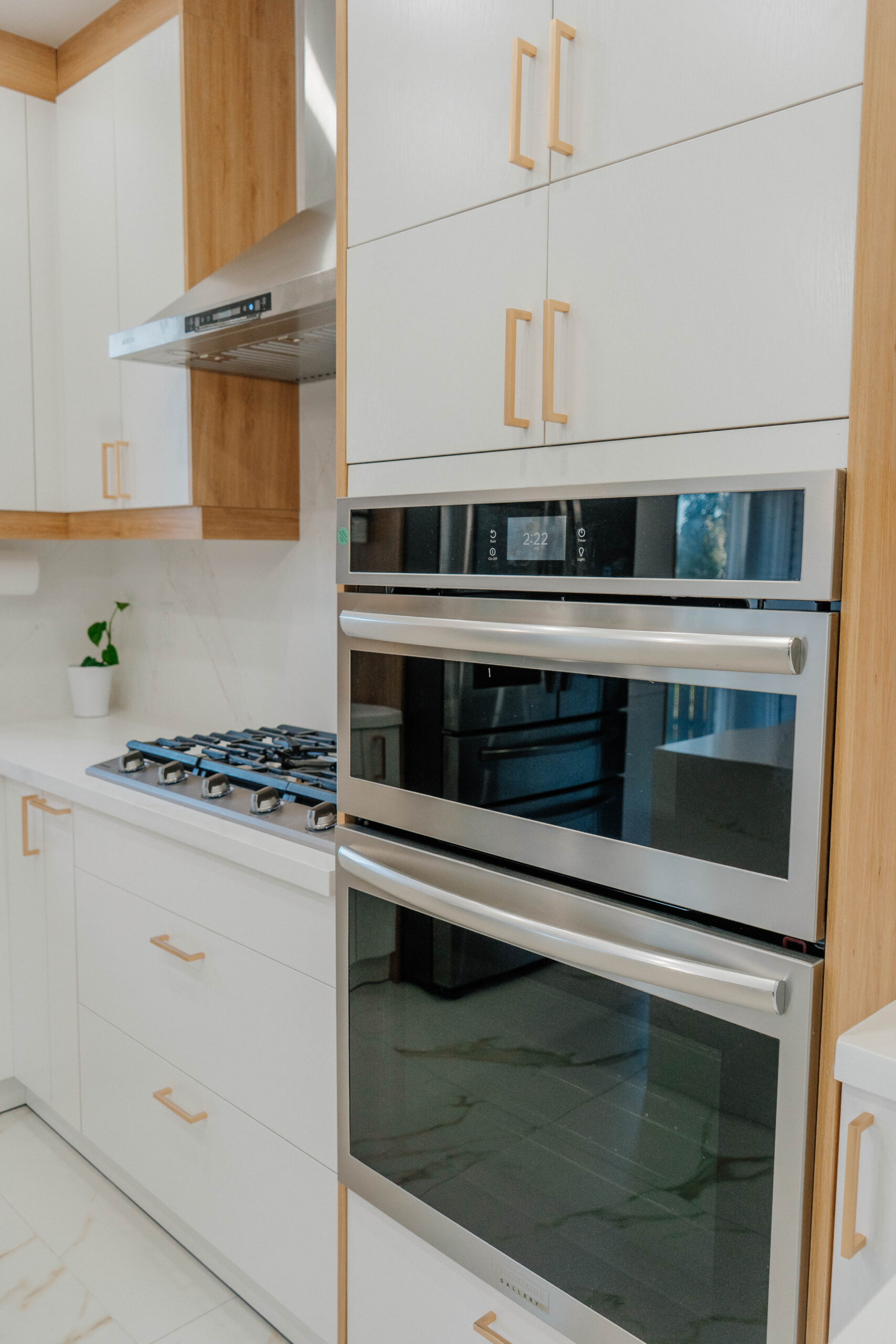 Detailed shot of the integrated stainless steel double wall oven and gas cooktop, surrounded by Matte White and Rustic Oak cabinets with gold hardware Pickering