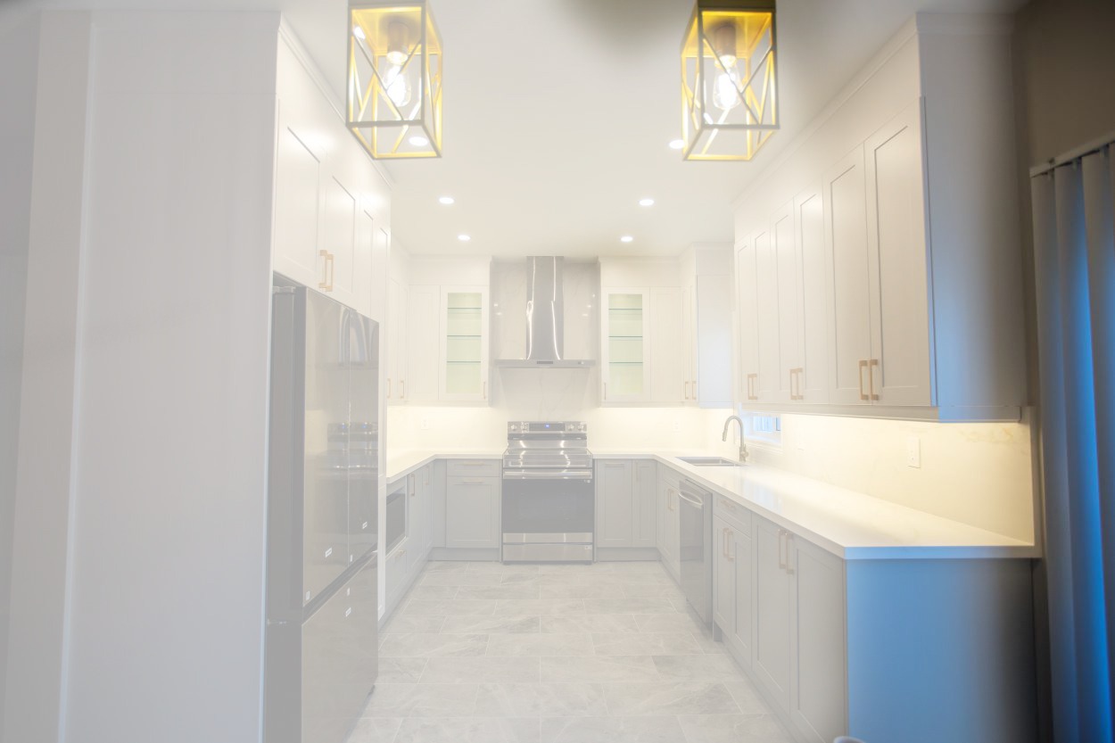 Modern U shaped kitchen renovation in Oakville featuring two tone matte white and light grey cabinetry with gold hardware, quartz countertops, elegant lighting, stainless steel appliances