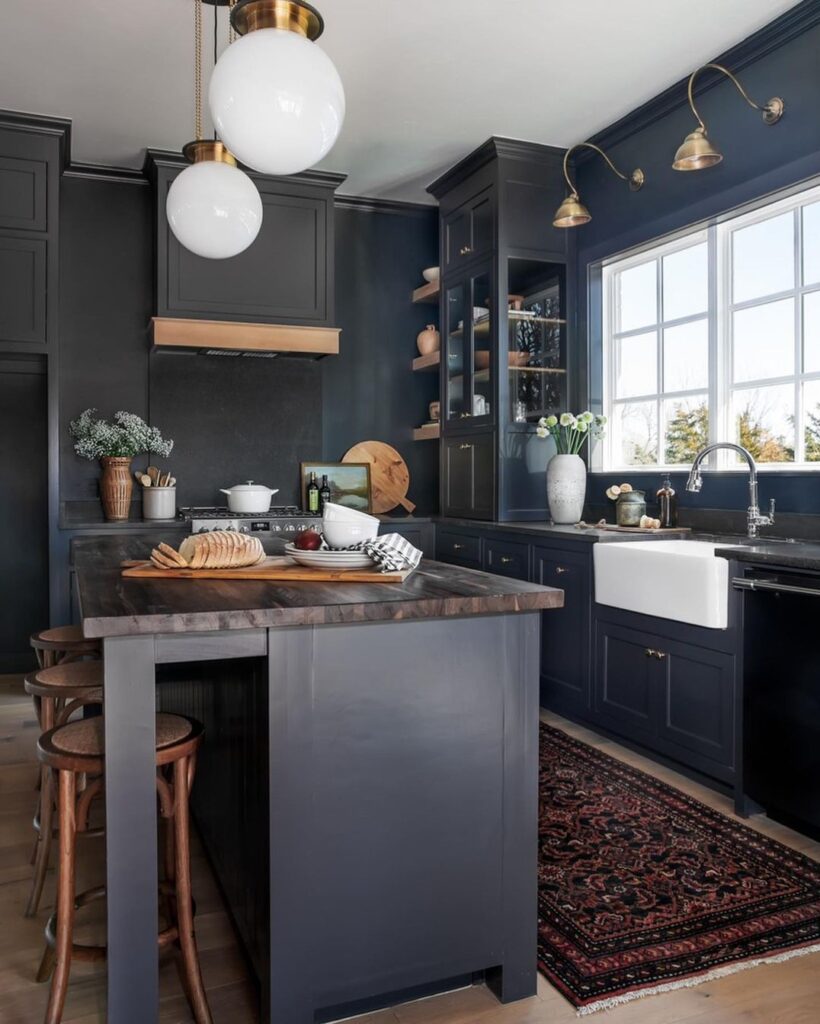 Moody dark blue kitchen perspective showing the thick wood island countertop, antique brass wall sconces, and Persian rug on light wood floor