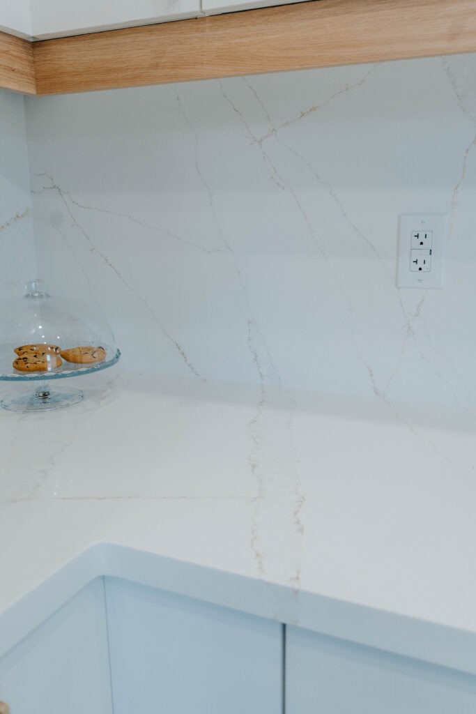 The Calacatta style quartz countertop transitions seamlessly into a full height backsplash, with a neatly integrated electrical outlet