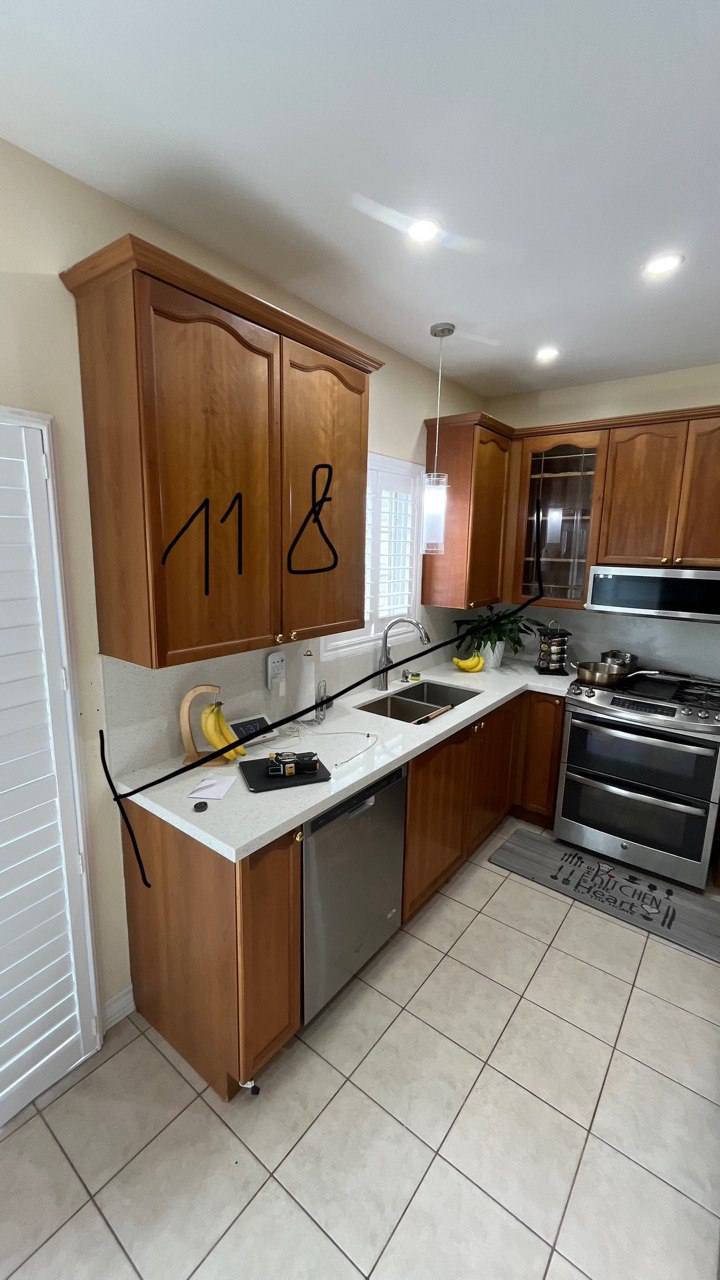The kitchen before the renovation, featuring traditional raised panel wood cabinets, a speckled white countertop, and beige tile flooring Pickering