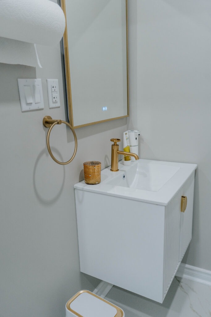 The new powder room features a white floating vanity with a gold faucet and towel ring, complemented by a modern LED backlit mirror