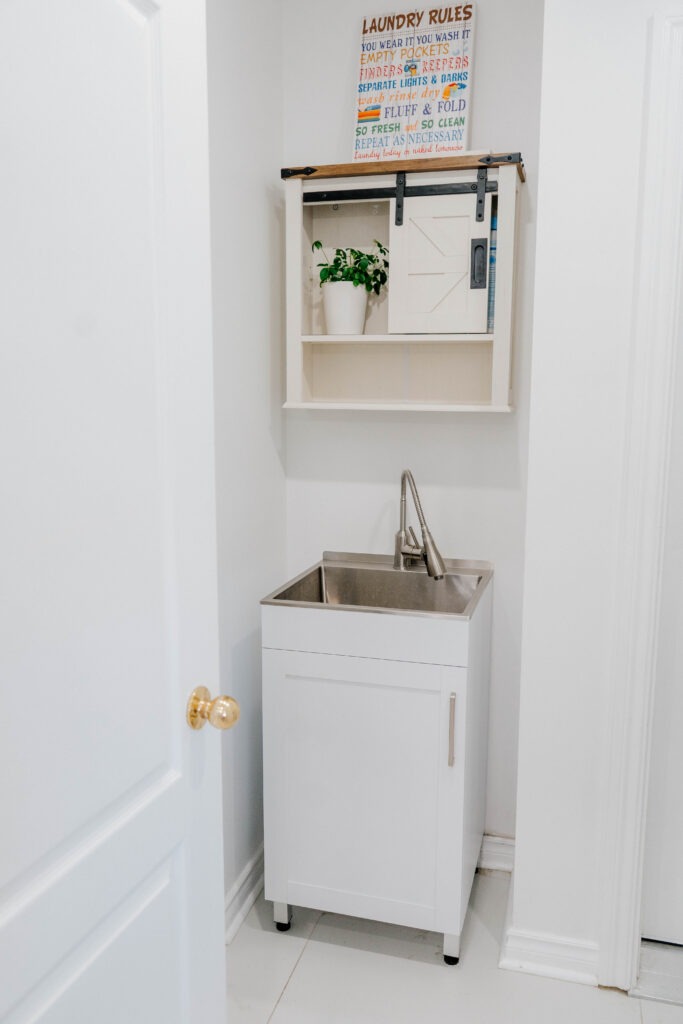 The updated laundry area features a functional white utility sink and a stylish wall cabinet with a modern farmhouse barn door