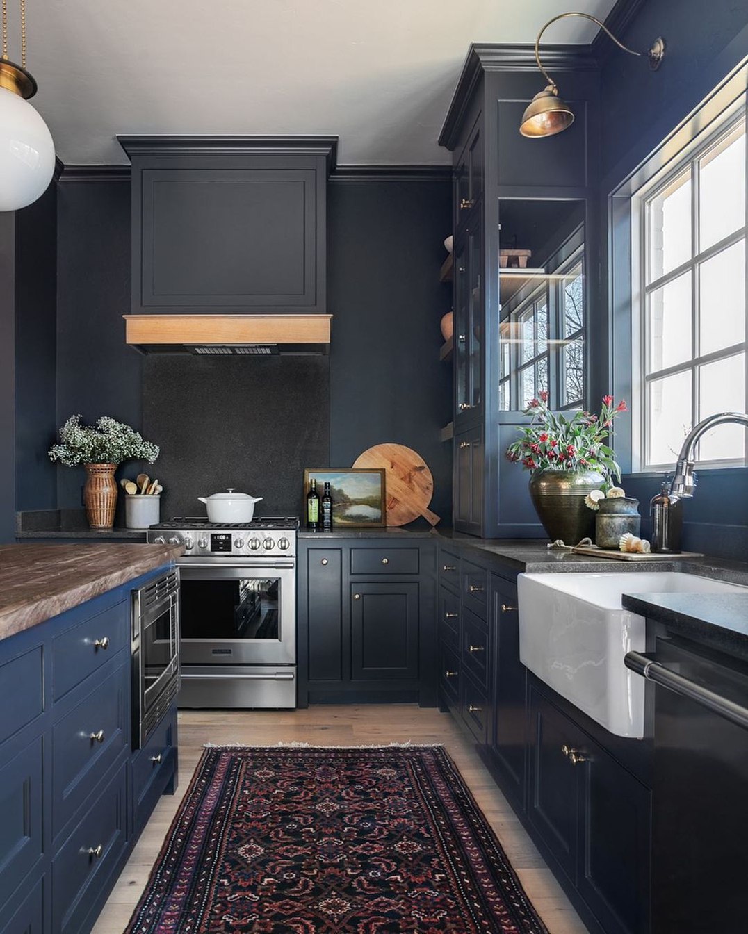 Traditional navy kitchen featuring a stainless steel range, custom chimney hood with a wood accent, and black stone backsplash Pickering