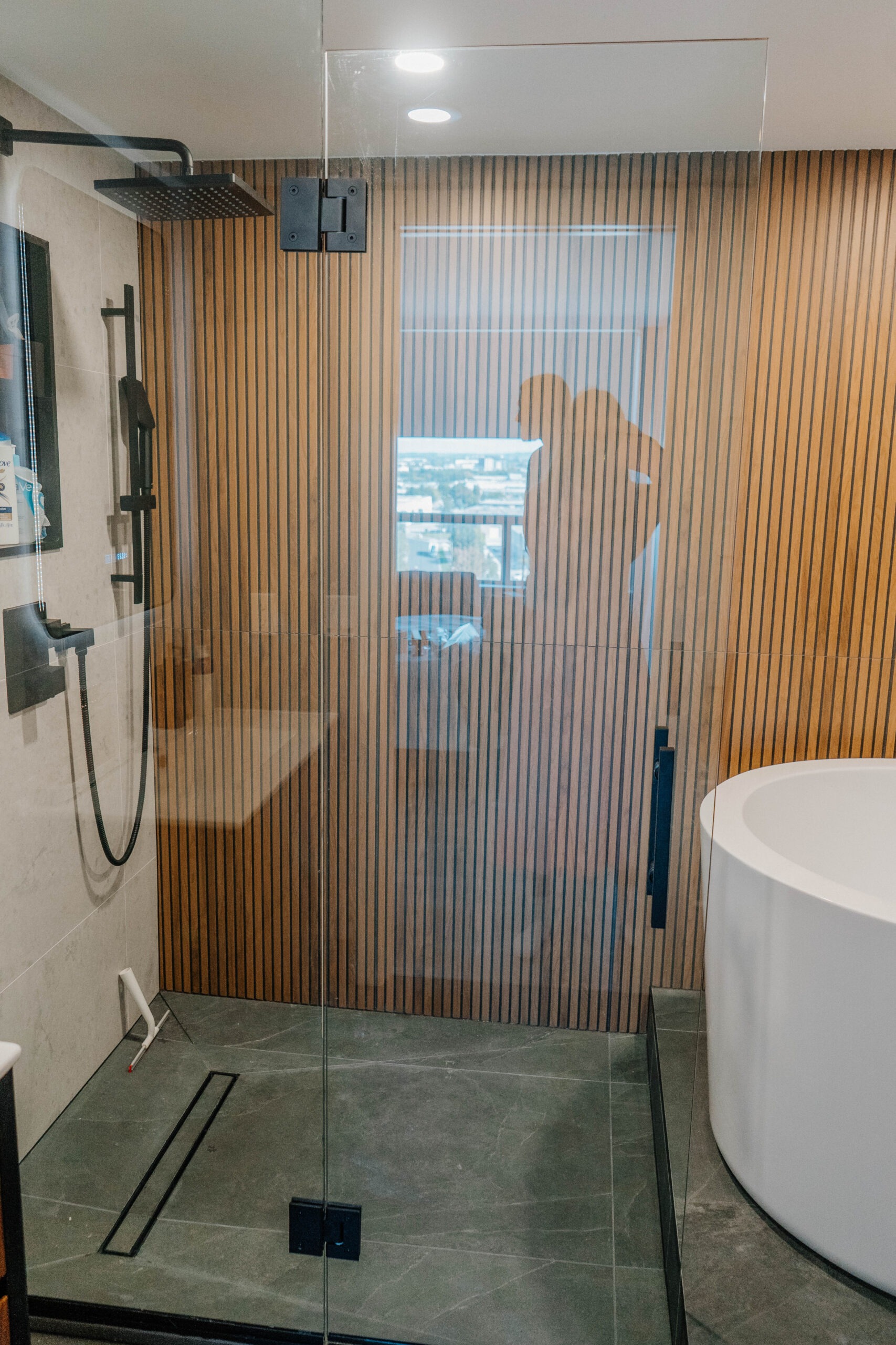Bathroom renovation in King City. Walk in shower with frameless glass, a vertical wooden slat accent wall, and a matte black rain shower. Modern bathroom renovation, Magic Reno design