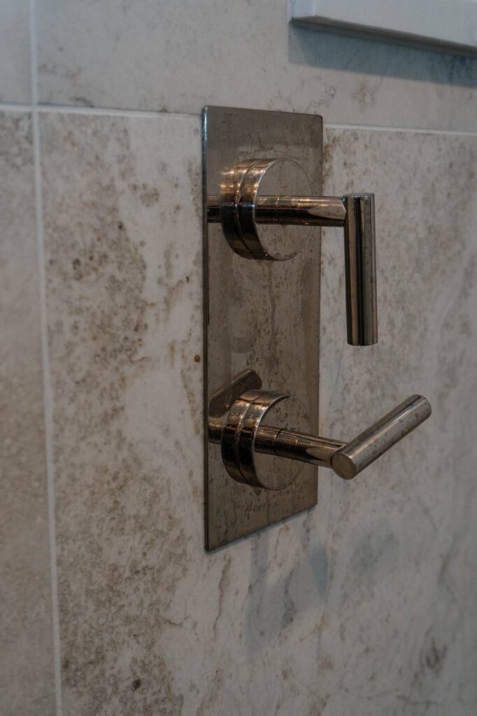Close up detail of modern chrome double robe hook mounted on beige marble look tile