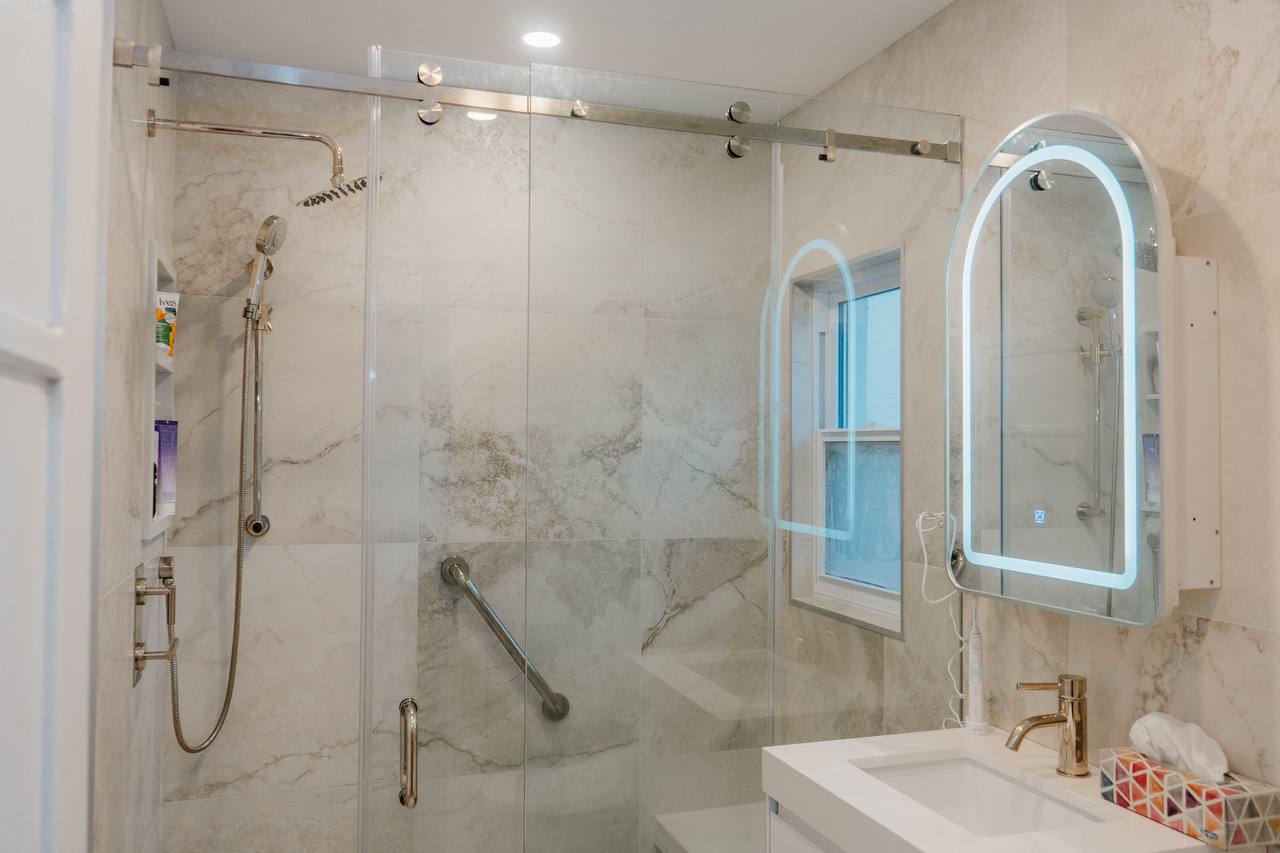 Full view of renovated bathroom with sliding glass shower door, marble tiles, and modern vanity