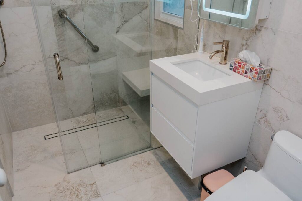Modern white floating vanity with gold faucet and arched LED medicine cabinet next to shower