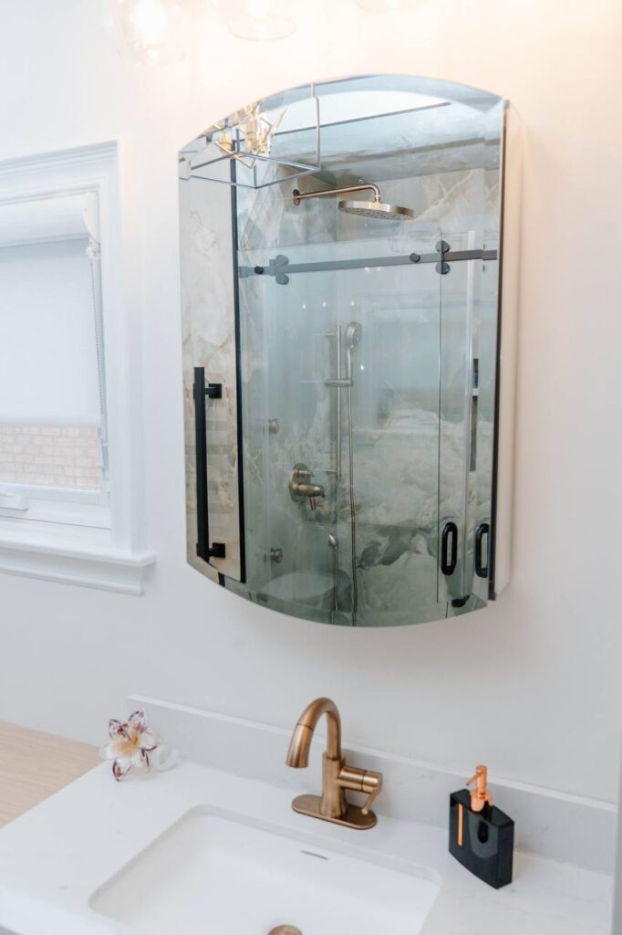 Reflection of porcelain slab ceiling and Delta rain shower head in a custom mirrored medicine cabinet