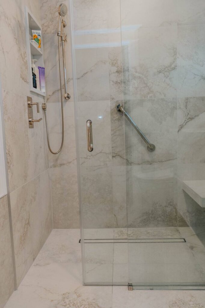 Shower interior featuring a chrome handheld spray, safety grab bar, and recessed tiled niche