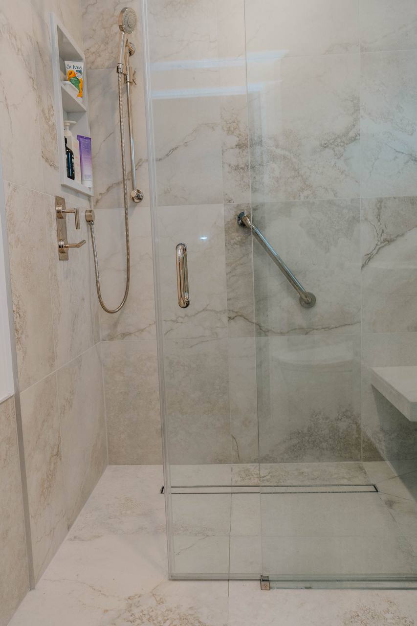 Bathroom Renovations in Oshawa Shower interior featuring a chrome handheld spray, safety grab bar, and recessed tiled niche Newmarket