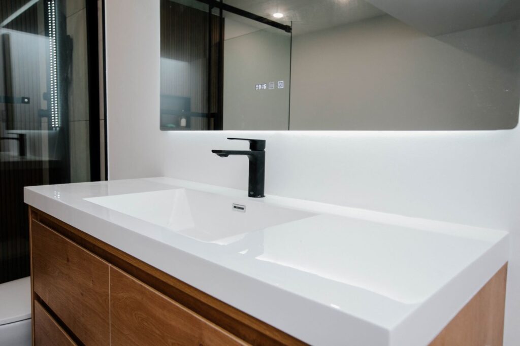 Close up of white integrated sink basin with a modern matte black single handle faucet and LED mirror reflectio