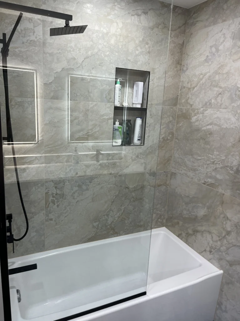 Deep soaking bathtub with frameless glass screen, warm beige marble porcelain tiles, and matte black shower system with double niche