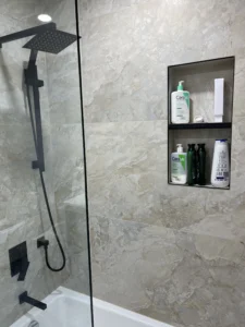 Detail of matte black rain shower head and tiled shampoo niche with black metal trim in a beige stone effect bathroom