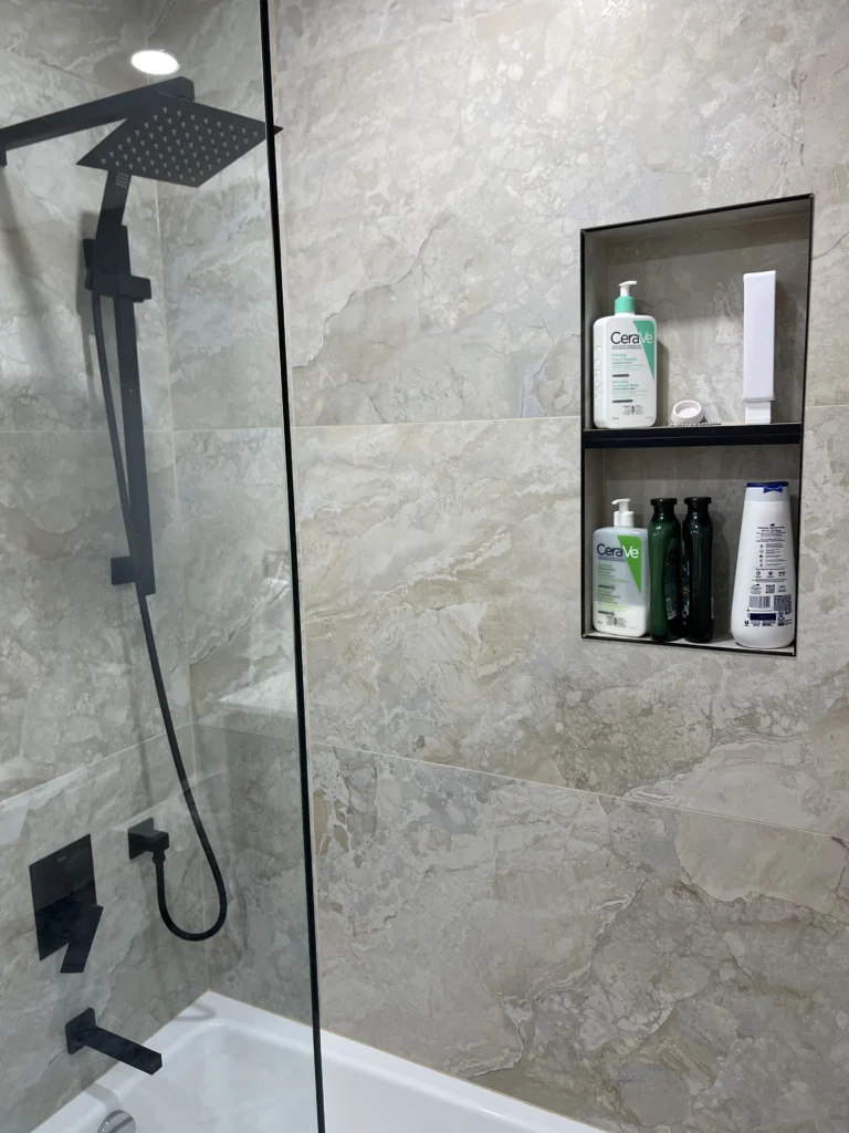 Detail of matte black rain shower head and tiled shampoo niche with black metal trim in a beige stone effect bathroom