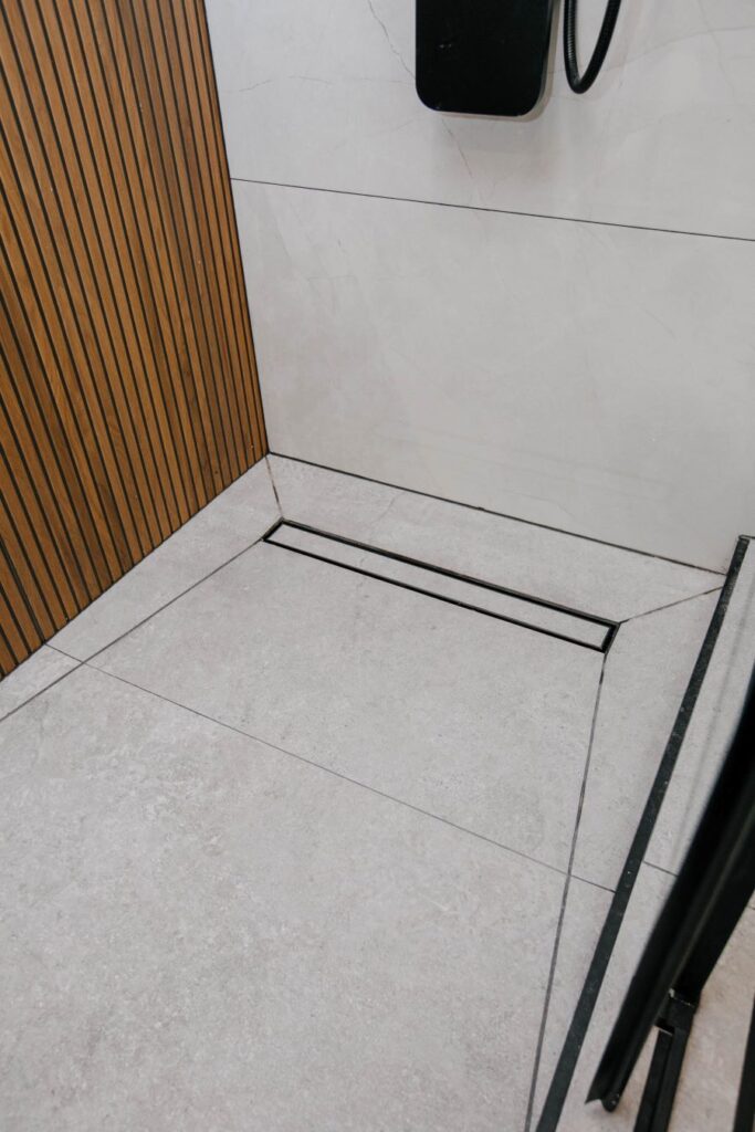 Detail of shower floor showing linear drain and the transition between wood slat wall tile and concrete look floor tile