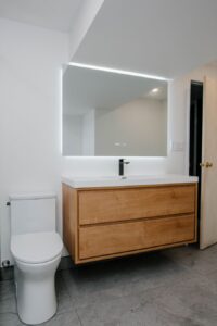 Powder room renovations in Toronto Floating wood vanity cabinet with white integrated sink and large LED backlit mirror with digital display