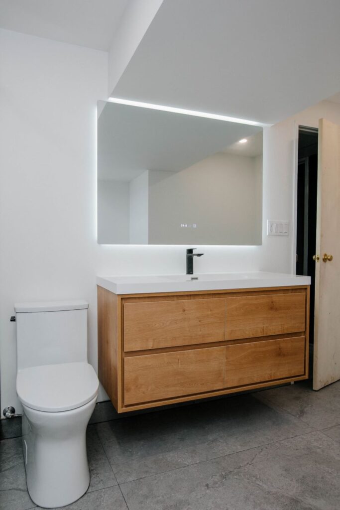 Floating wood vanity cabinet with white integrated sink and large LED backlit mirror with digital display
