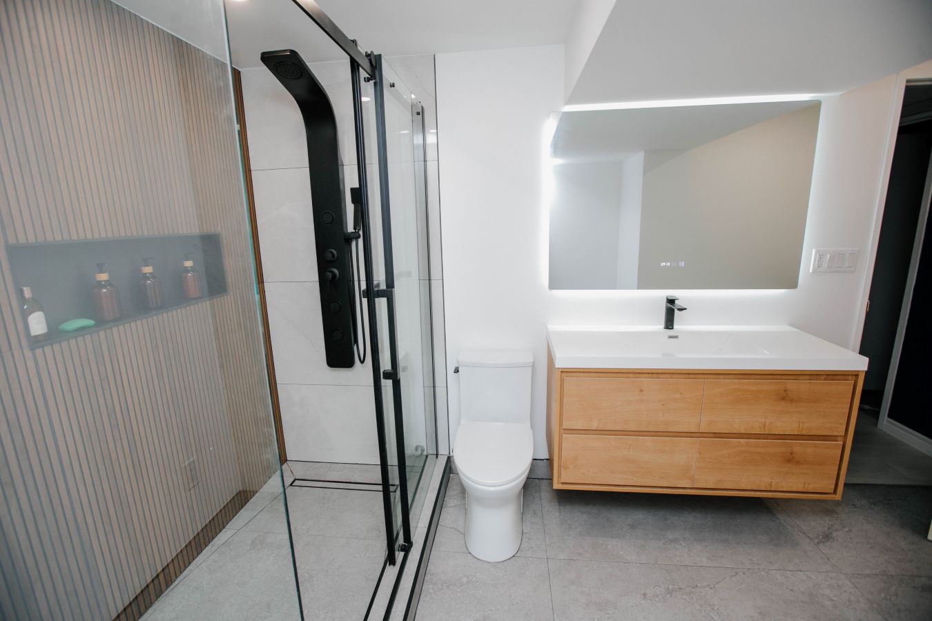 Full view of modern bathroom featuring a wood slat shower, black sliding glass doors, white toilet, and floating wood vanity with LED mirror