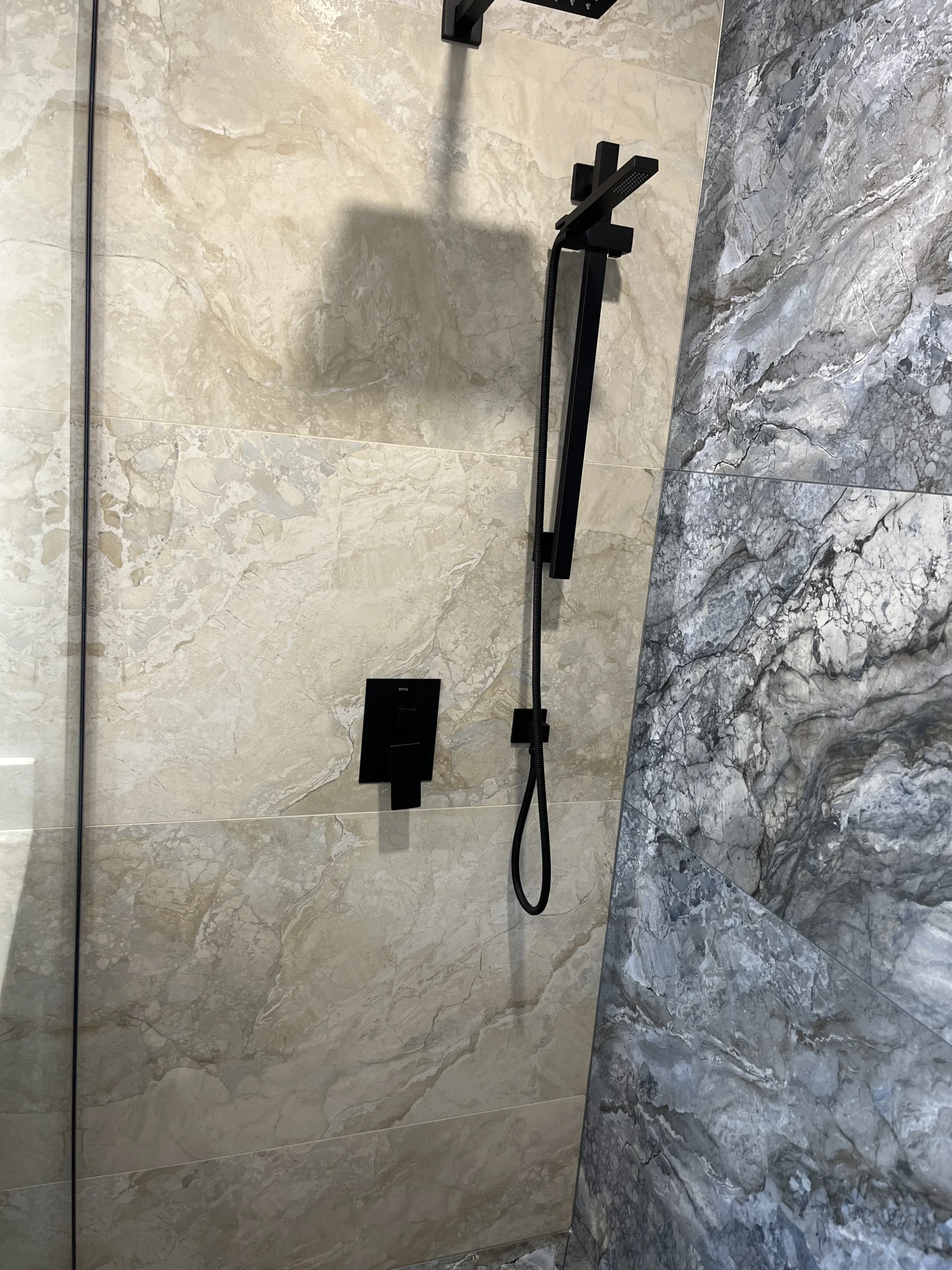 Matte black shower rail and mixer valve installed on beige marble large format tiles
