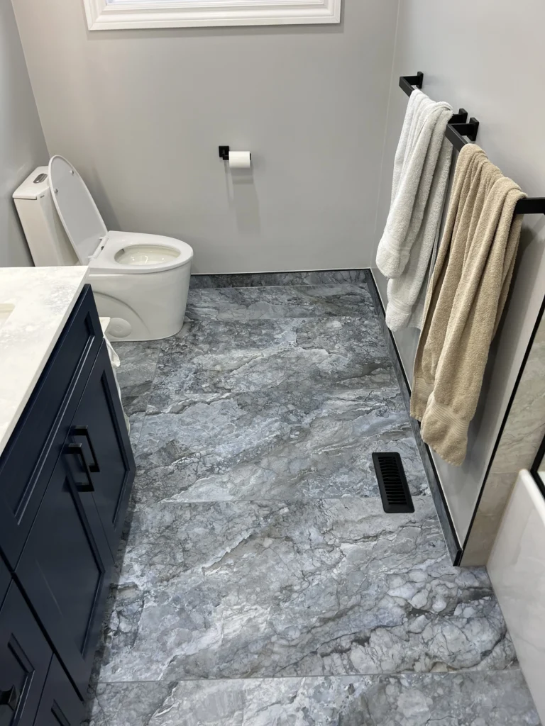 Modern bidet toilet installed against blue grey marble porcelain tiles with matte black towel warmer above